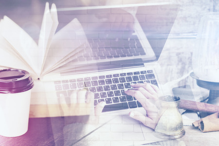Close up of woman's hands using laptop placed on desktop with open book,  coffee cup and other items. Student concept. Double exposureの写真素材