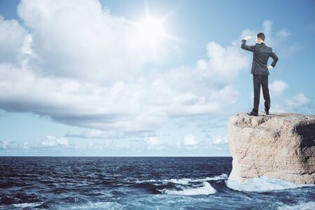 Businessman standing on rock and looking into the distance on ocean background. Research conceptの写真素材