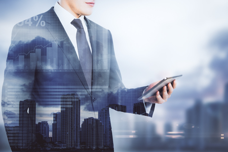 Businessman using cellphone on blurry city background with copy space and business charts. Technology concept. Double exposure