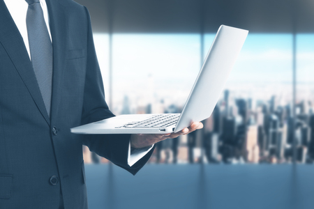 Businessman holding notebook on blurry office background with city view. Communication conceptの写真素材