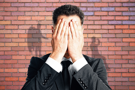 Businessman with angel and demon shadows on red brick wall background. True personality conceptの写真素材