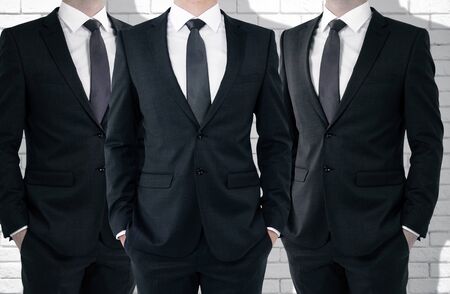 Three unrecognizable businessmen on white brick wall background. Partnership concept