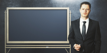 Handsome european businessman with empty blackboard on concrete wall background. Education and information concept. Mock up, 3D Renderingの写真素材