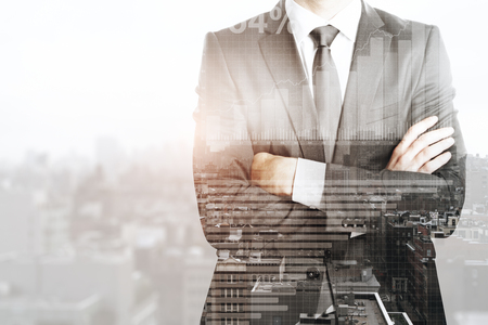 Unrecognizable businessman with folded arms standing on abstract city background with forex chart. Income concept. Double exposureの写真素材