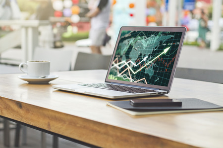 Side view of laptop with forex chart placed on wooden cafe table wit coffee cup and other items. Blurry street background. Analysis conceptの写真素材