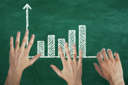 Abstract image of hands with drawn business chart on chalkboard background. Teamwork and savings concept の写真素材