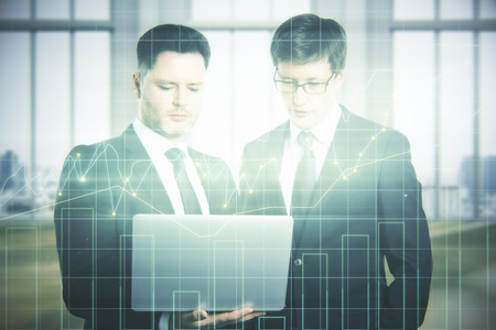 Portrait of two handsome businessmen using laptop together in blurry office interior with abstract forex chart. Economy concept. Double exposure の写真素材