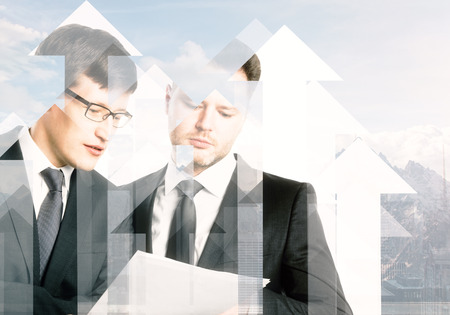 Handsome european businessmen disucssing contract together on abstract city background with arrows and sunlight. Partnership and investment concept. Double exposure の写真素材