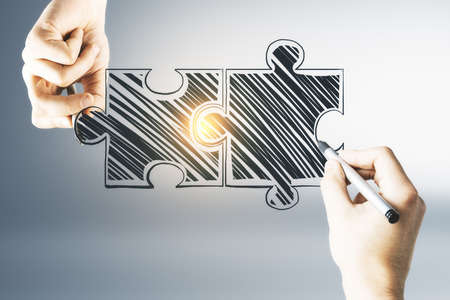 Hands holding and drawing glowing puzzle pieces on light background. Teamwork and success conceptの写真素材