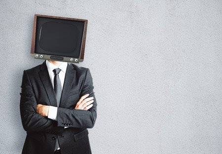 TV headed businessman with folded arms standing on concrete wall background. Mock upの写真素材
