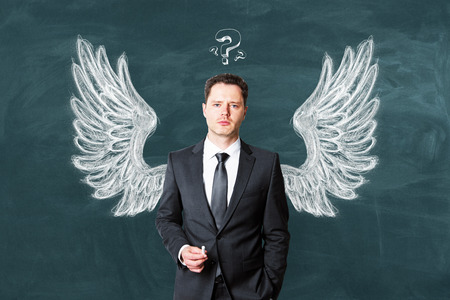 Handsome european businessman on chalkboard background with drawn wings. Leadership and support conceptの写真素材