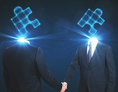 Puzzle headed businessmen shaking hands on blue background. Teamwork and success conceptの写真素材