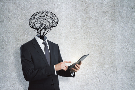 Brain headed businessman with tablet standing on concrete wall background. Brainstorm and technology conceptの写真素材
