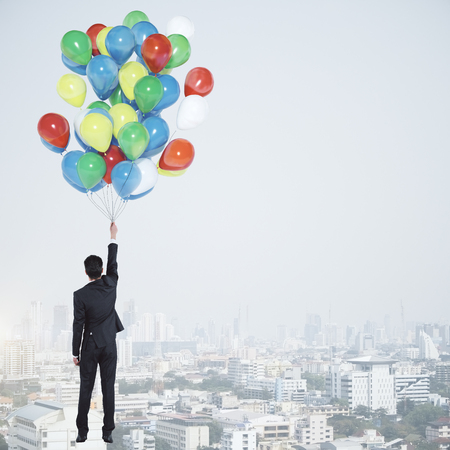 Businessman flying with balloons on abstract cloudy sky and city background with copy space. Success and inspiration conceptの写真素材
