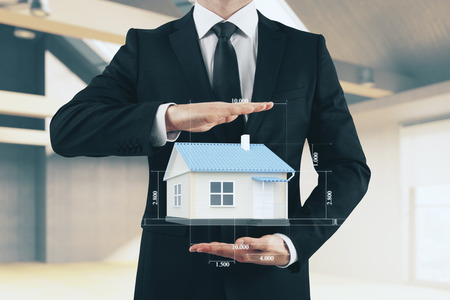 Businessman holding creative house blueprint on blurry office interior background. Architect and rent conceptの写真素材
