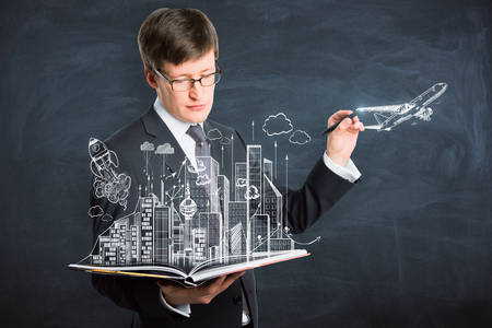 Handsome european businessman drawing creative education, city, travel, startup sketch on chalkboard backgroundの写真素材