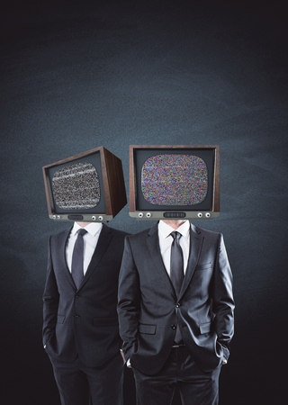 TV headed businessmen standing on concrete wall background. Brainwash and control concept の写真素材