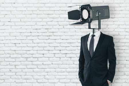 Spotlight headed man standing on empty white brick wall background with copy space. Professional conceptの写真素材