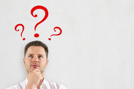 Thinking businessman with drawn question marks standing on concrete wall background. Confusion and ask concept の写真素材