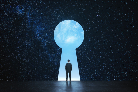 Back view of young businessman standing against keyhole door on starry sky background. Dream, success, opportunity and access conceptの写真素材