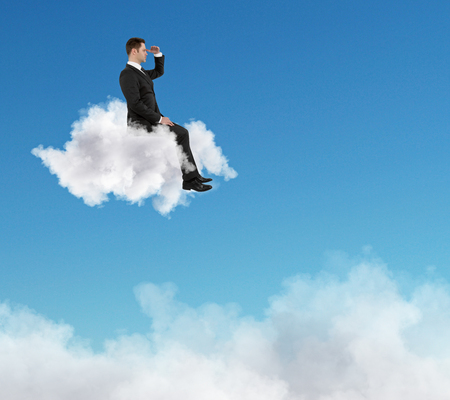 success concept with businessman sitting on a cloud and staring into the distance at blue sky background.の写真素材