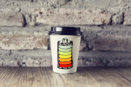 need coffee concept with coffee paper mug displayed as low battery icon on wooden table at brick wall background. 3D renderingの写真素材