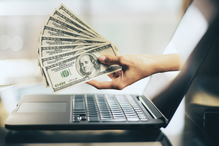 Hand with dollars sticking out of laptop screen. Cryptocurrency and investment conceptの写真素材