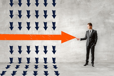 Businessman drawing red arrow on concrete wall background. Leadership and success concept