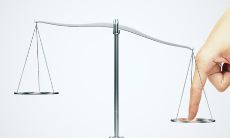 Tip the scales of justice concept. Finger illegaly influencing the legal system for an unfair advantage on white background.の写真素材