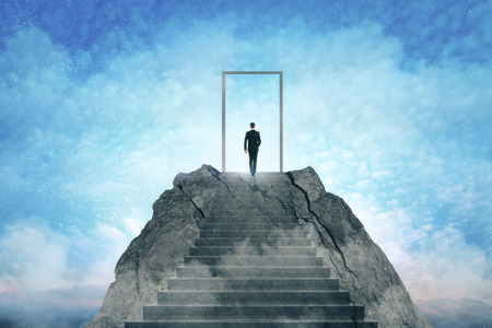 Businessman standing on abstract mountain with door on sky background. Promotion and dream conceptの写真素材