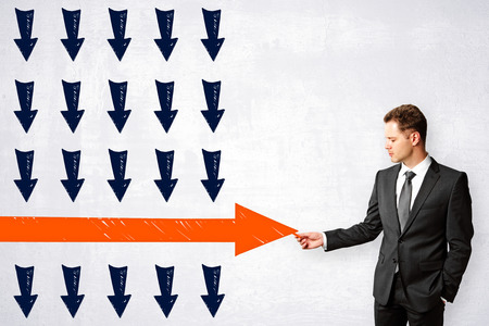 Businessman drawing red arrow on concrete wall background. Leadership and way conceptの写真素材