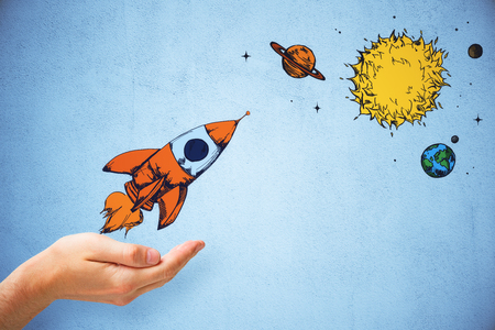 Hand holding creative rocket sketch on concrete wall background. Startup and planet conceptの写真素材