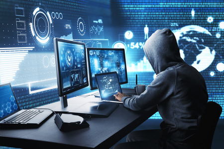 Side view of hacker using computer with digital interface while sitting at desk of blurry interior....