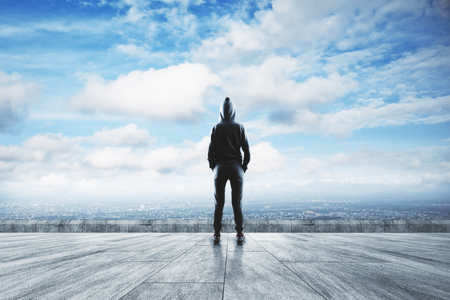 Young hacker standing on concrete rooftop with city and sky view. Criminal and research conceptの写真素材