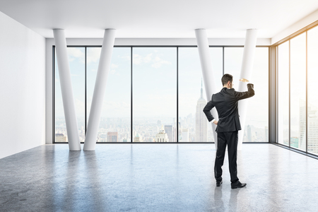 Businessman standing and looking into the distance in empty concrete interior with panoramic city view. Research concept. 3D Renderingの写真素材