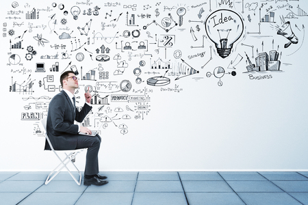 Side view of young businessman sitting on chair in interior with business sketch. Success and idea conceptの写真素材