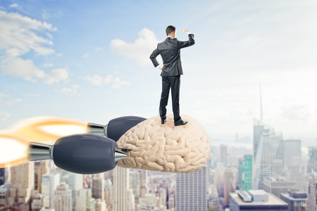 Businessman looking into the distance on abstract launching brain rocket. Sky and city background. Brainstorm and success concept. 3D Renderingの写真素材