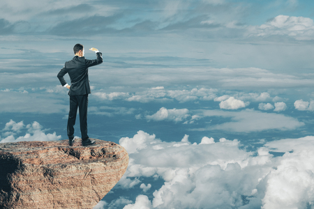 Back view of young businessman looking into the distance on cliff and beautiful sky background. Research and occupation conceptの写真素材