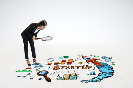 Attractive young european businesswoman using binoculars to look at business sketch on floor. Startup and research conceptの写真素材