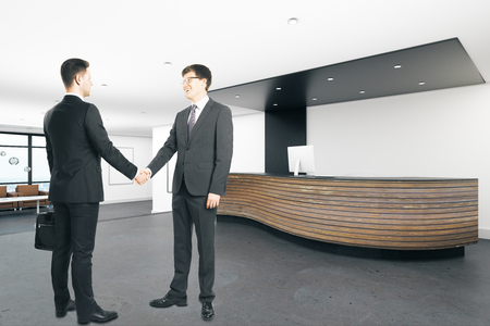 Two handsome european businessmen shaking hands in modern office interior. Teamwork and coworkers concept. 3D Renderingの写真素材