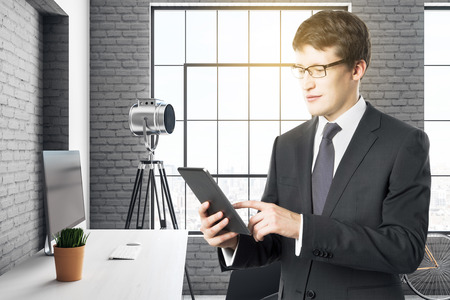 Attractive young european businessman using tablet in modern loft office interior. Technology and communication concept. 3D Renderingの写真素材