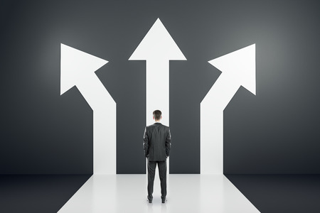 Back view of young businessman standing on black background with three arrows. Different direction and success conceptの写真素材