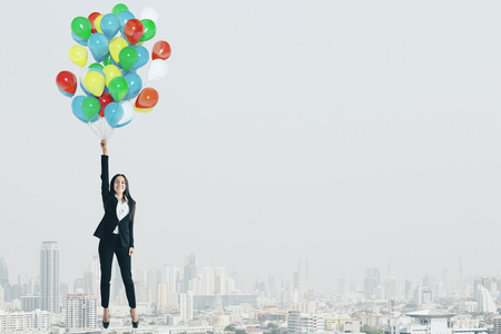 Attractive cheerful young businesswoman flying with colorful balloons on sky background. Freedom and success conceptの写真素材