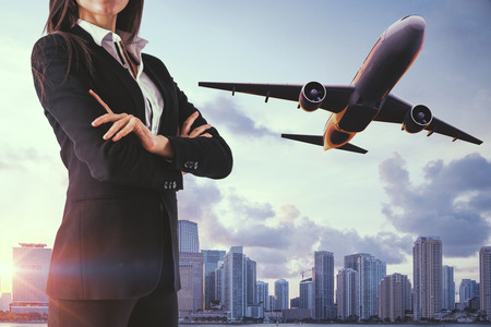Attractive young businesswoman on sky city background with flying airplane. Success, travel and work conceptの写真素材