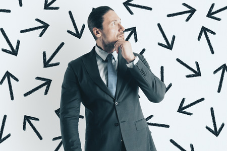Portrait of thoughtful young european businessman with arrows. Way and direction conceptの写真素材
