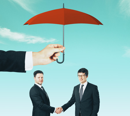 Businessmen working together under red umbrella on bright blue sky background. Teamwork and protection conceptの写真素材