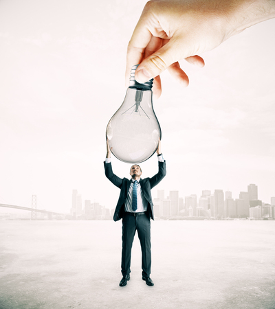 Hand handing lamp to businessman on abstract city background. Idea and teamwork conceptの写真素材