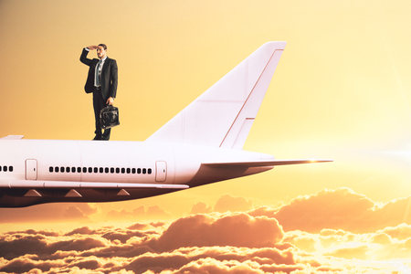 Businessman looking into the distance on abstract airplane and sunset sky background. Transportation and research concept.の写真素材