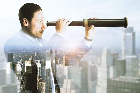Side view of young businessman using binoculars to look into the future on abstract city background. Vision and career concept. Double exposureの写真素材