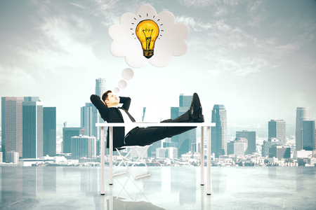 Relaxing young businessman at desk thinking about bright idea on rooftop city background. Innovation and solution conceptの写真素材